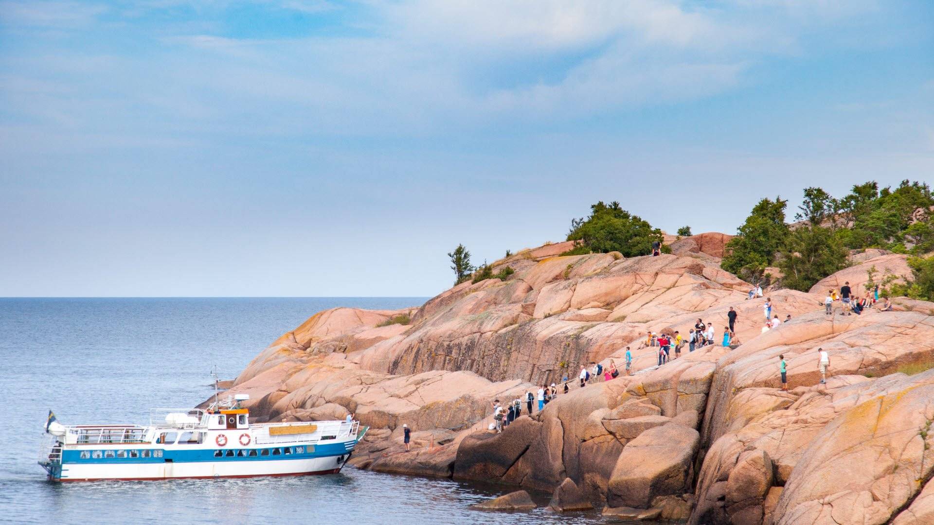 Besökare på väg att gå ombord på en båt för hemfärd från Blå jungfrun. De vandrar nerför en klippavsats. Blå jungfrun nationalpark.